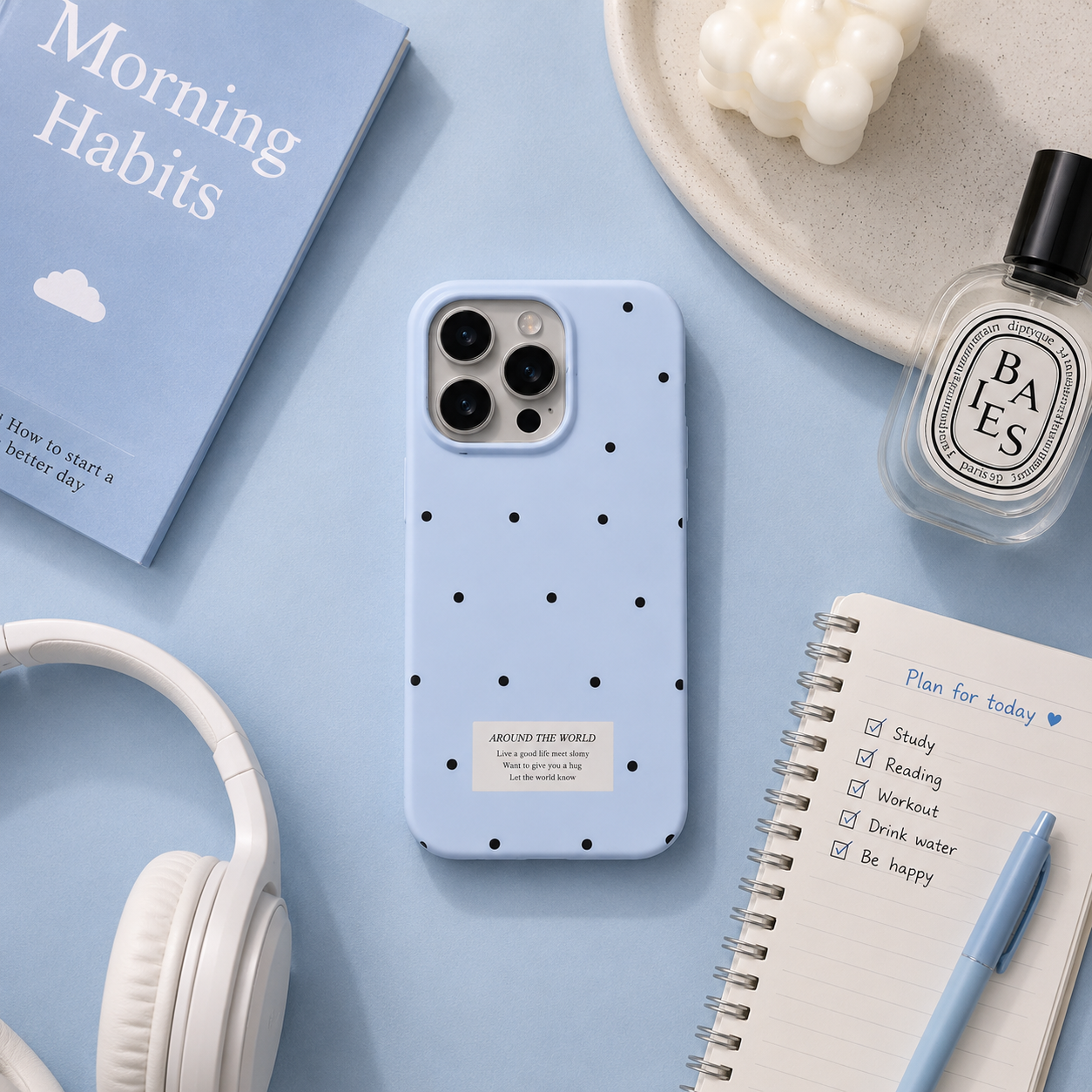 Blue phone case with black polka dots on a light blue surface with accessories like headphones and a notebook.
