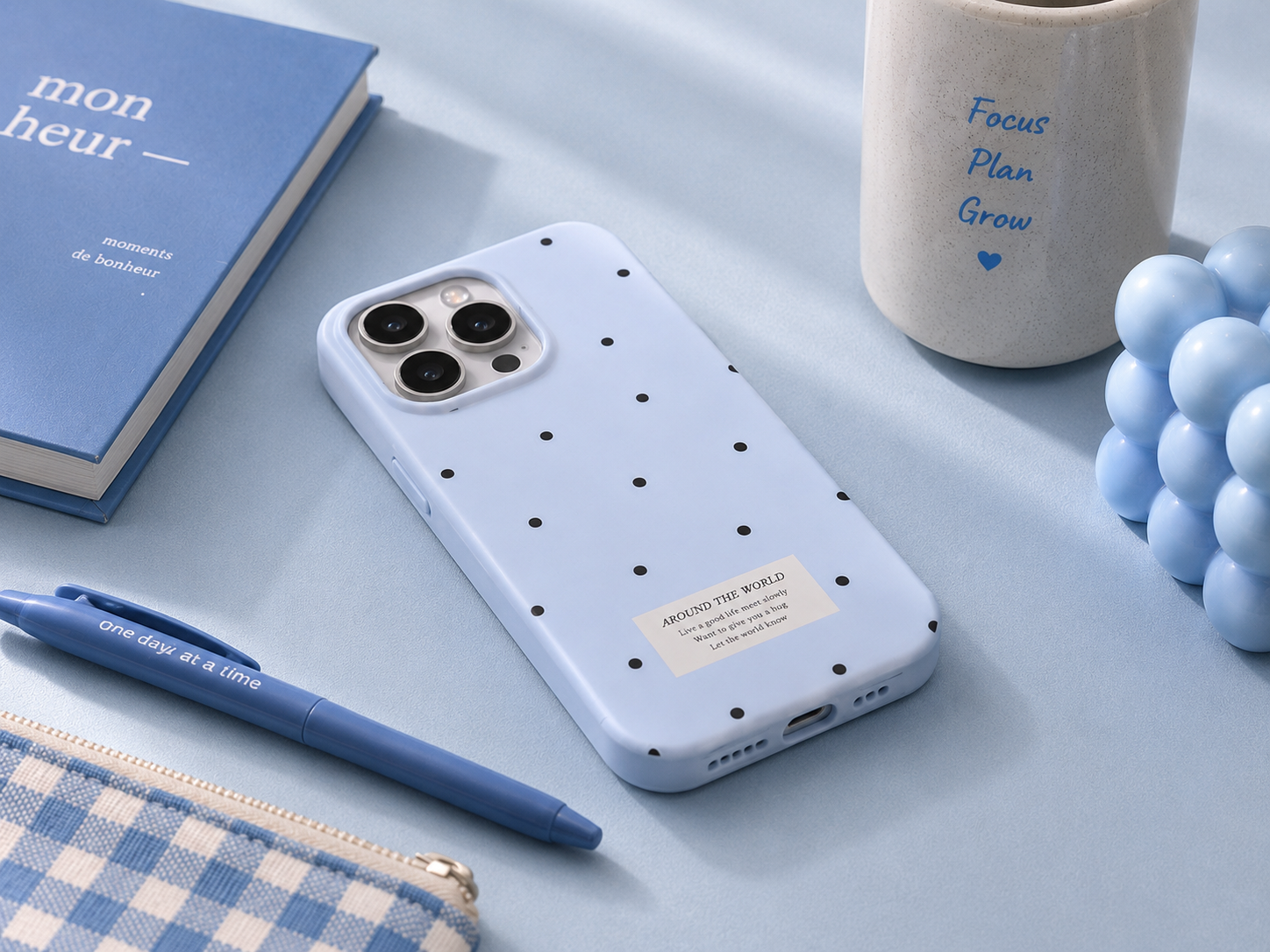 Blue phone case with black polka dots on a light blue surface with accessories like headphones and a notebook.